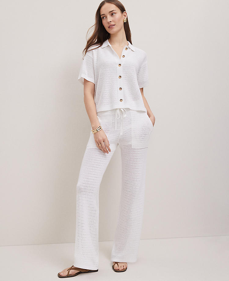 A woman wearing a white mesh sweater with a collared neckline and buttons, paired with matching wide-leg mesh pants, standing against a plain background.