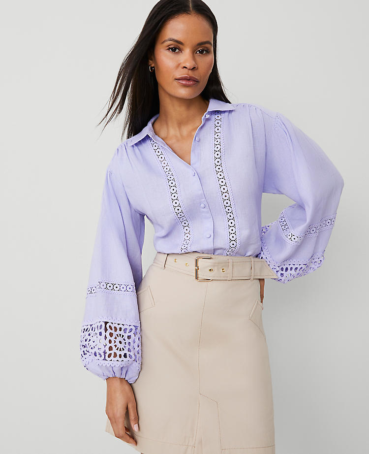 A woman wearing a light lavender embroidered linen blouse with puff sleeves, shirred shoulders, and a shirttail hem.