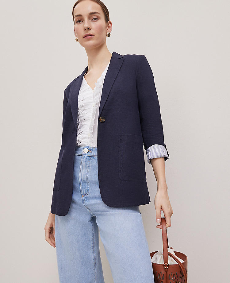 A woman wearing a navy blue linen-blend blazer with roll-up sleeves, notched lapels, and patch pockets, paired with light blue jeans.