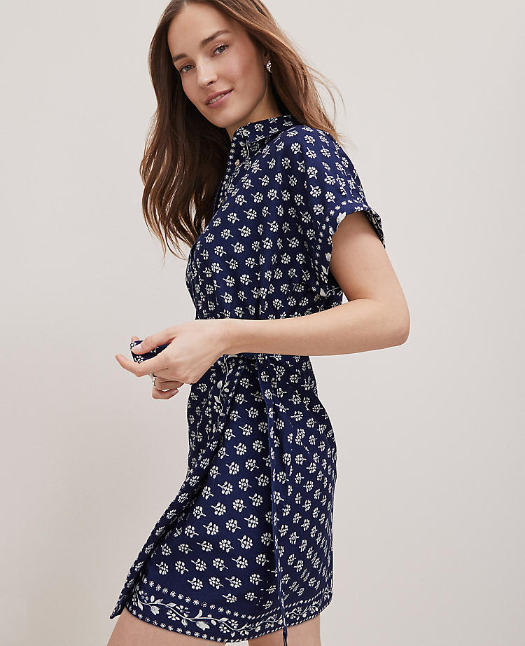 A woman wearing a navy blue floral wrap shirtdress with short dolman sleeves, a point collar, and front buttons.