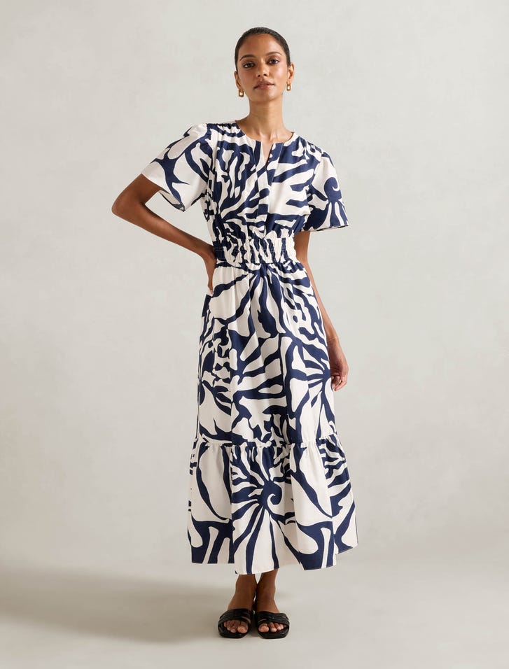 A woman wearing a navy and white abstract print midi dress with a V-neckline, short flounce sleeves, and an elasticized waist, standing against a plain background.