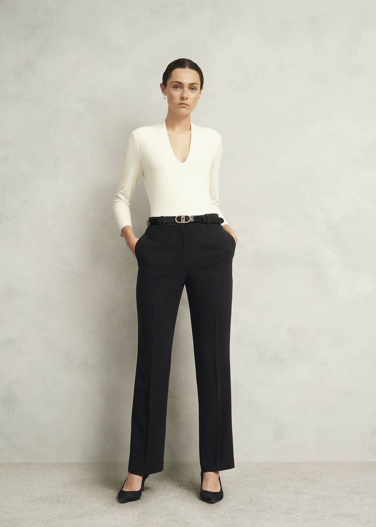 A woman wearing black straight trousers with a crepe finish, paired with a white top and black heels.