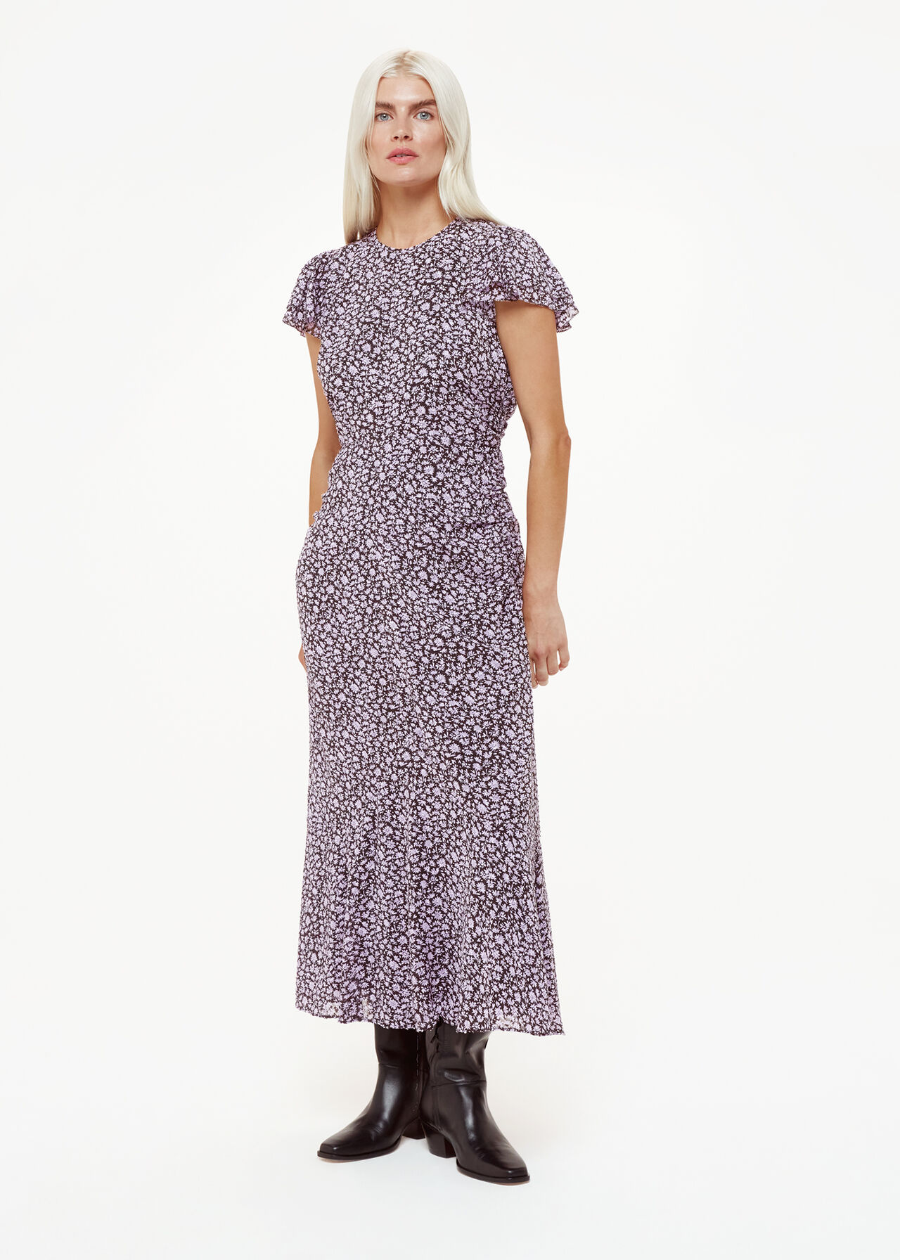 A woman wearing a purple midi dress with a daisy print, gathered waist, and flutter sleeves, paired with black boots.