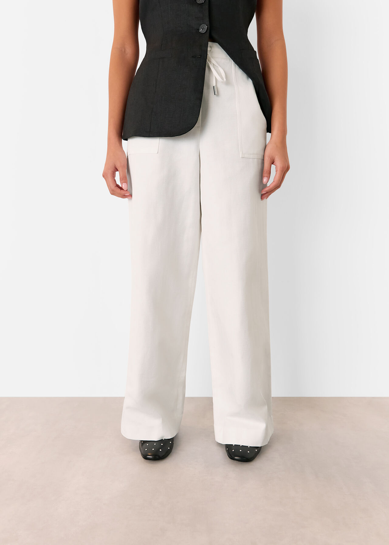 A woman wearing white linen-blend trousers with a wide-leg cut, elastic waistband with a drawstring, and large front pockets.