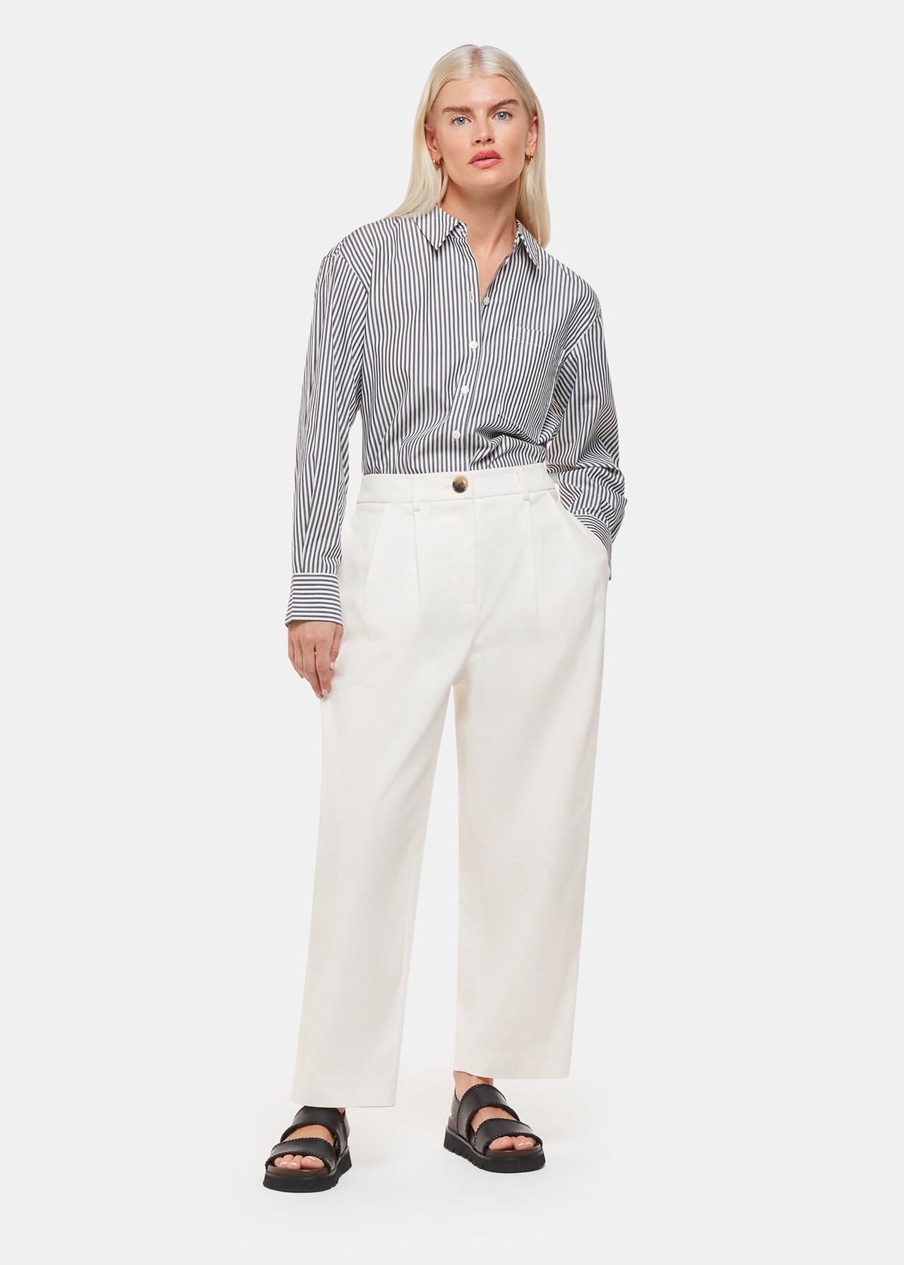 A woman wearing white trousers with a high waist, barrel leg shape, front pleats, and side pockets, paired with a striped shirt.