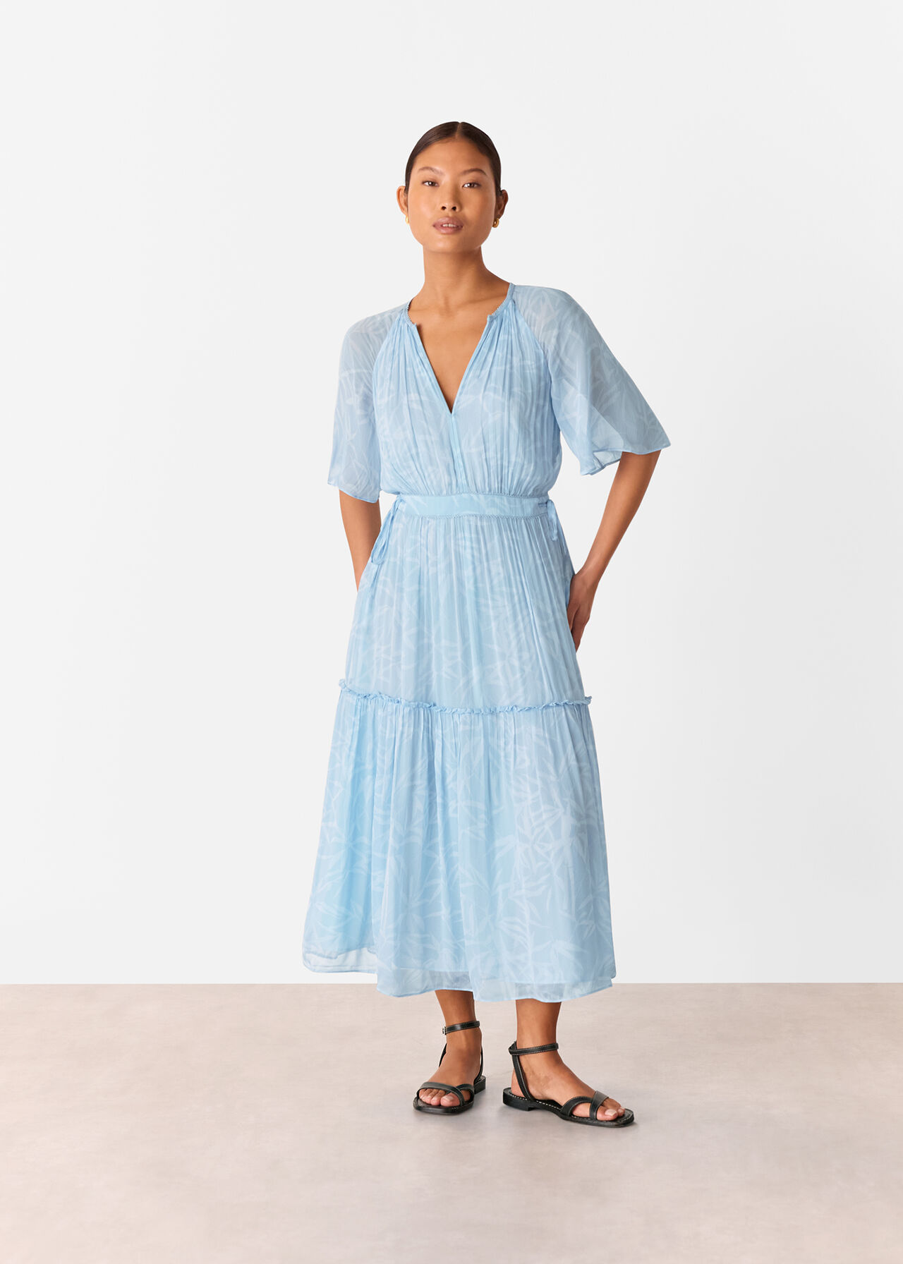 A woman wearing a light blue dress with bamboo leaf patterns, scalloped V-neckline, frills, short raglan sleeves, and a gathered waist.