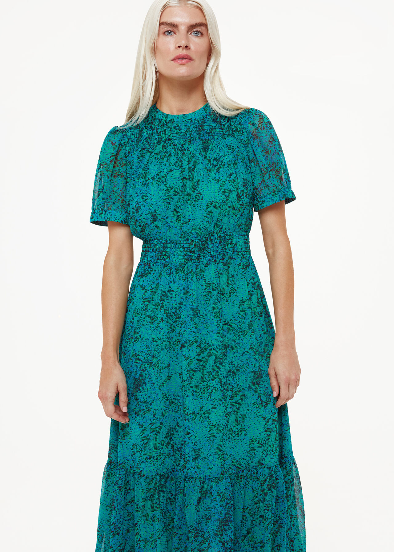 A woman wearing a teal dress with a diagonal snake print, fitted bodice, high round neck, midi length, and slightly puffed sleeves.