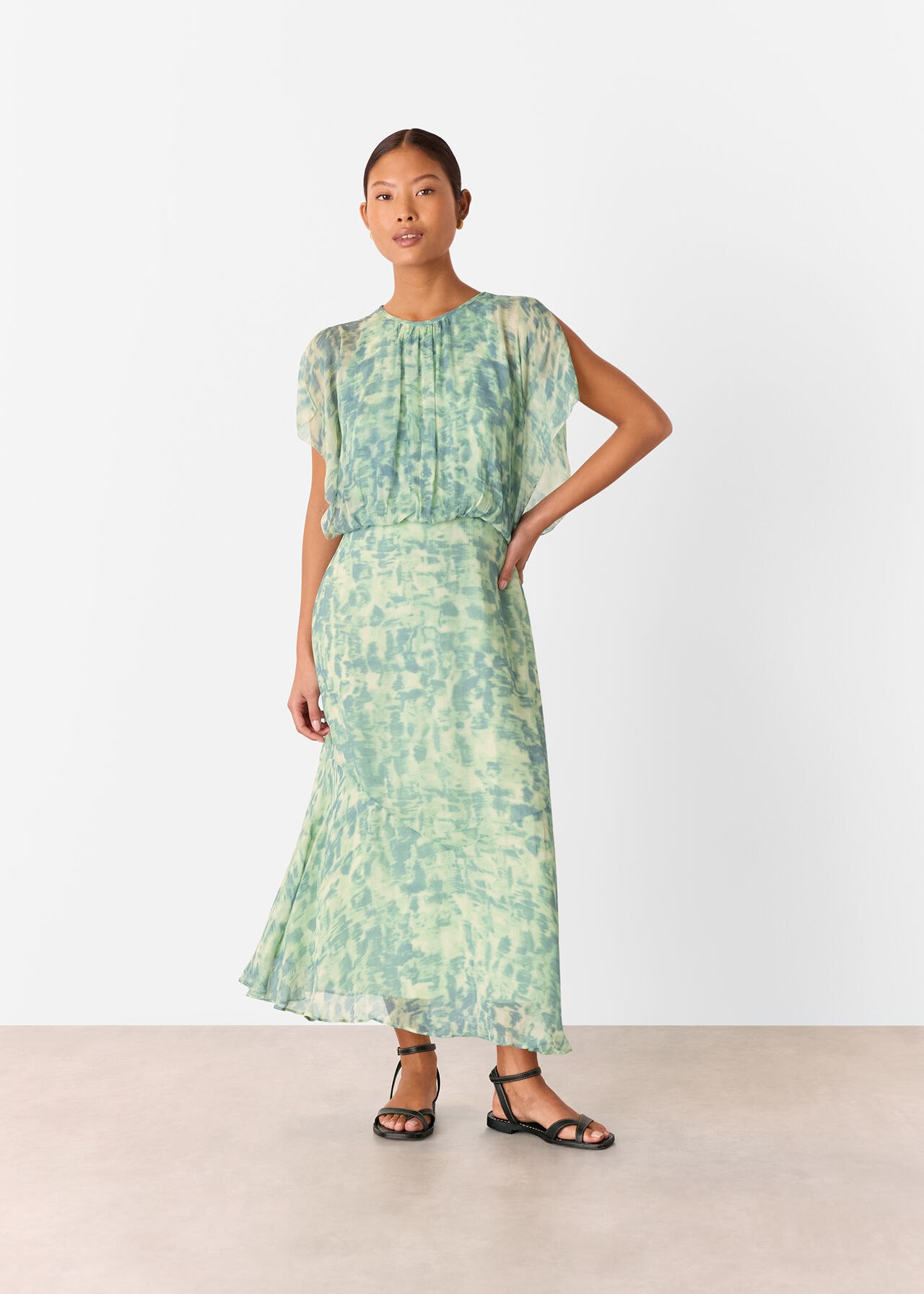 A woman wearing a green midi dress with dashed brush marks pattern, waterfall sleeves, round neckline, and cinched waist.