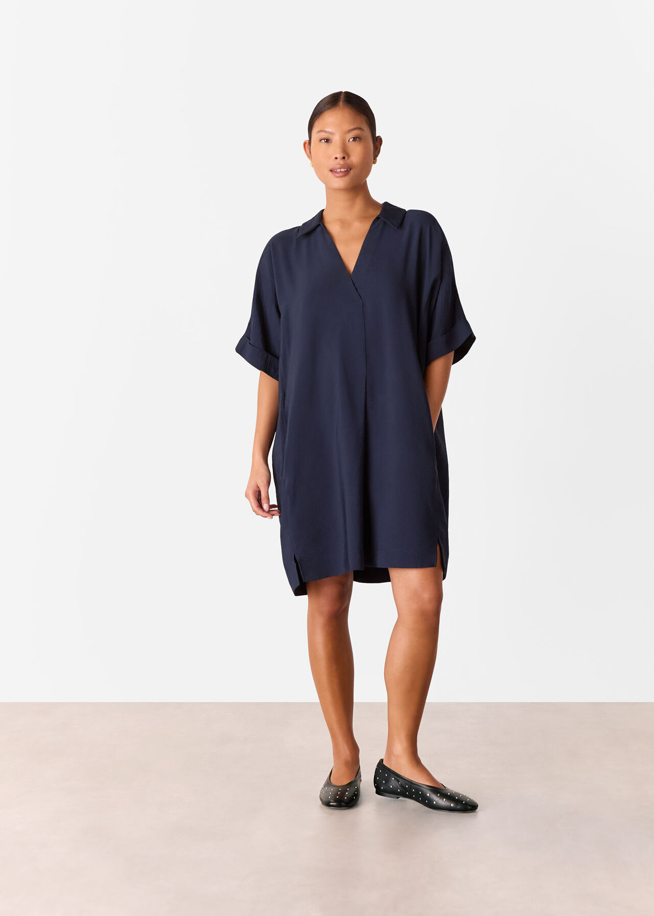 A woman wearing a navy petite Melanie dress with a relaxed cocoon shape, V-neckline, short rolled-up sleeves, and side slits, standing against a plain background.