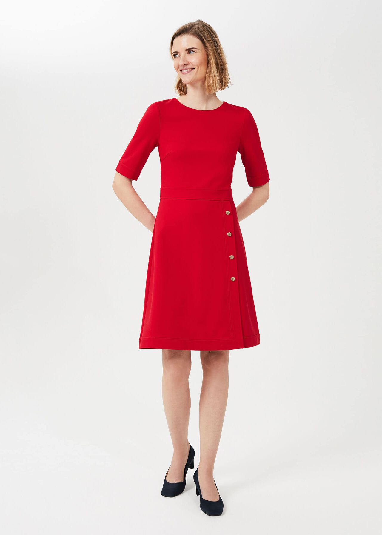 A woman wearing a red dress with ballet sleeves, a faux wrap skirt, and gold buttons, standing against a plain background.