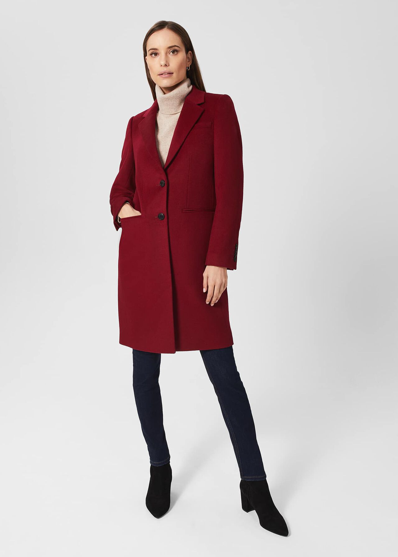 A woman wearing a deep red, tailored, single-breasted wool coat with seam detailing and a Melton undercollar, standing against a plain background.