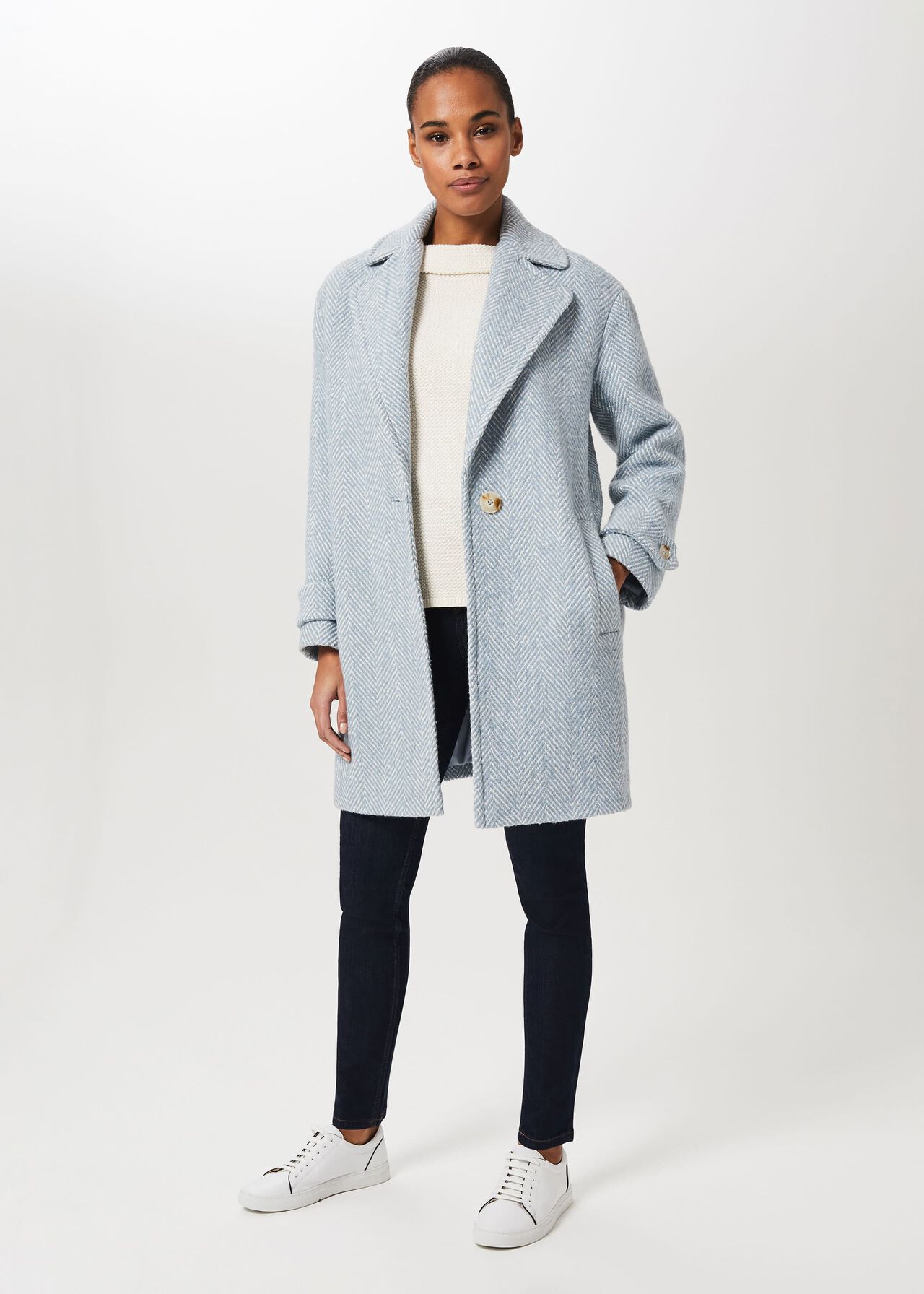 A woman wearing a grey petite herringbone coat with a relaxed fit, single button closure, and dropped shoulders, paired with a cream sweater, black jeans, and white sneakers.