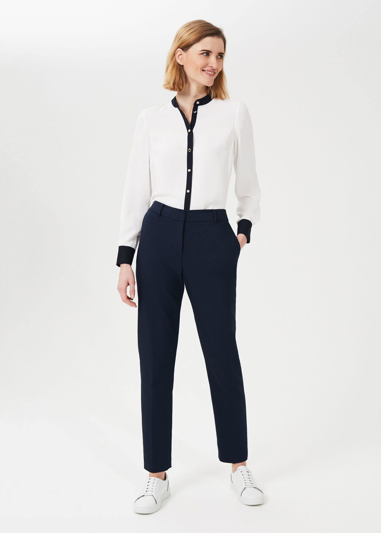 A pair of navy blue tapered trousers with belt loops and pocket details, worn by a woman in a white and navy blouse.