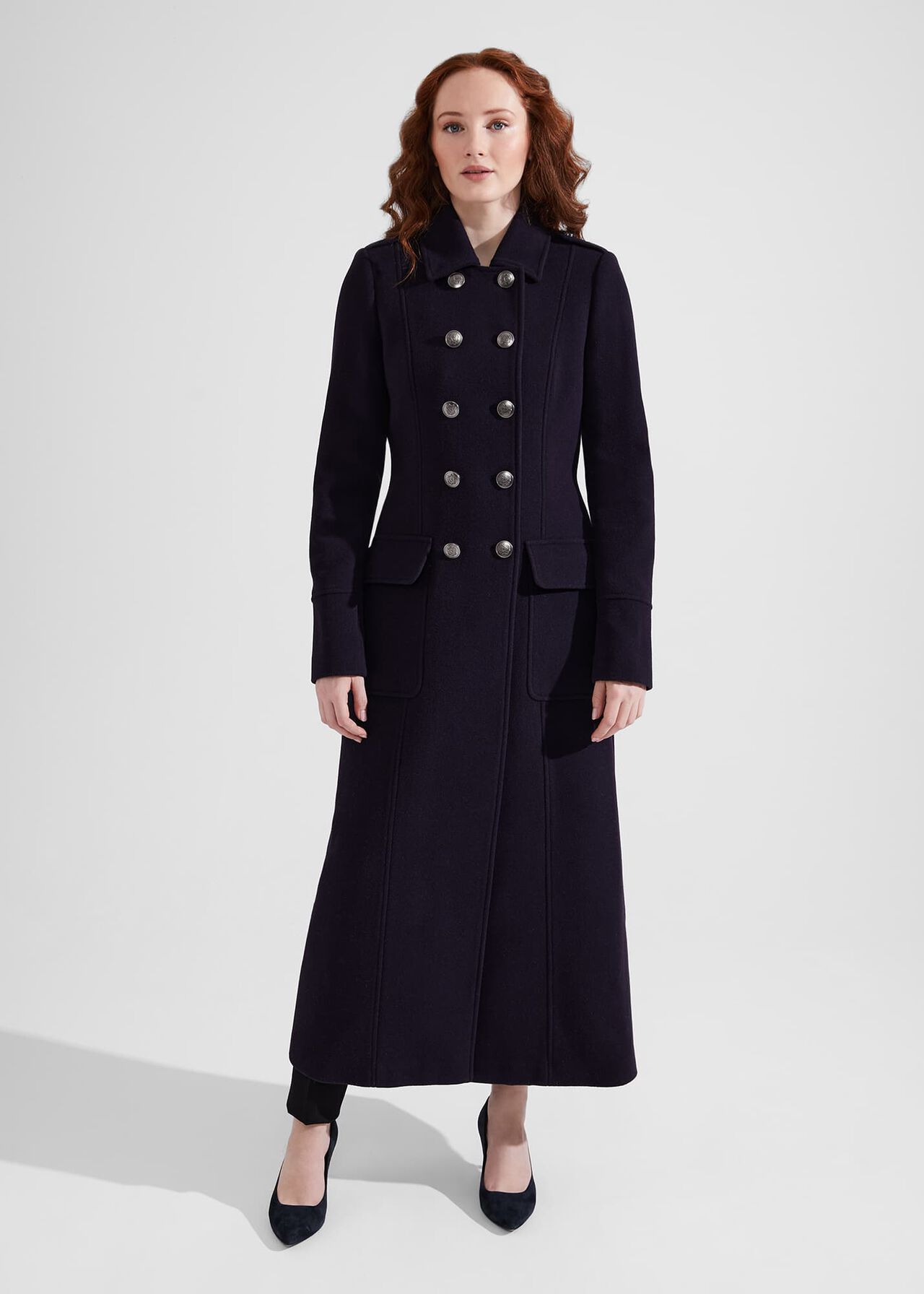 A woman wearing a navy blue, long, double-breasted wool maxi coat with metallic buttons, a collar, and flap pockets.