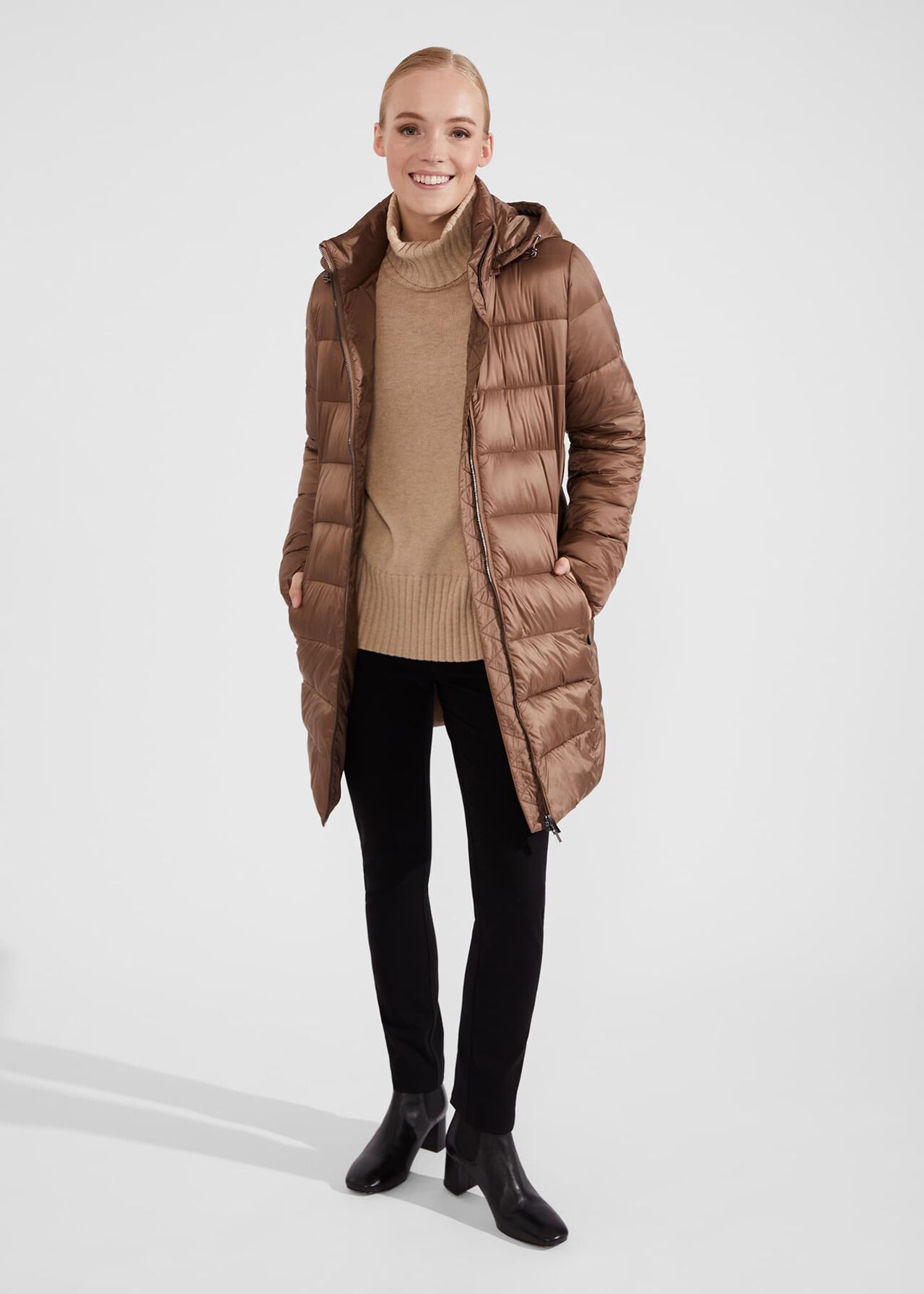 A woman wearing a brown hooded puffer coat with a front zipper, side pockets, and a hood, standing against a plain background.