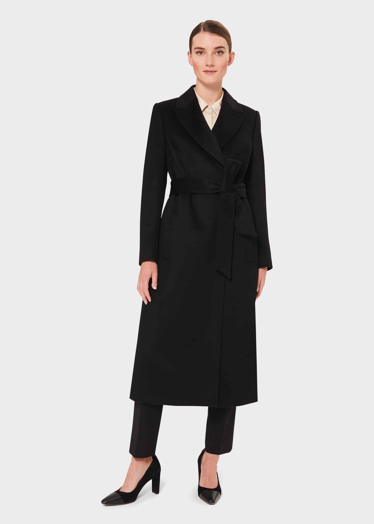A woman wearing a black wool wrap coat with lapels, a belt, and a midi length, paired with black pants and heels.