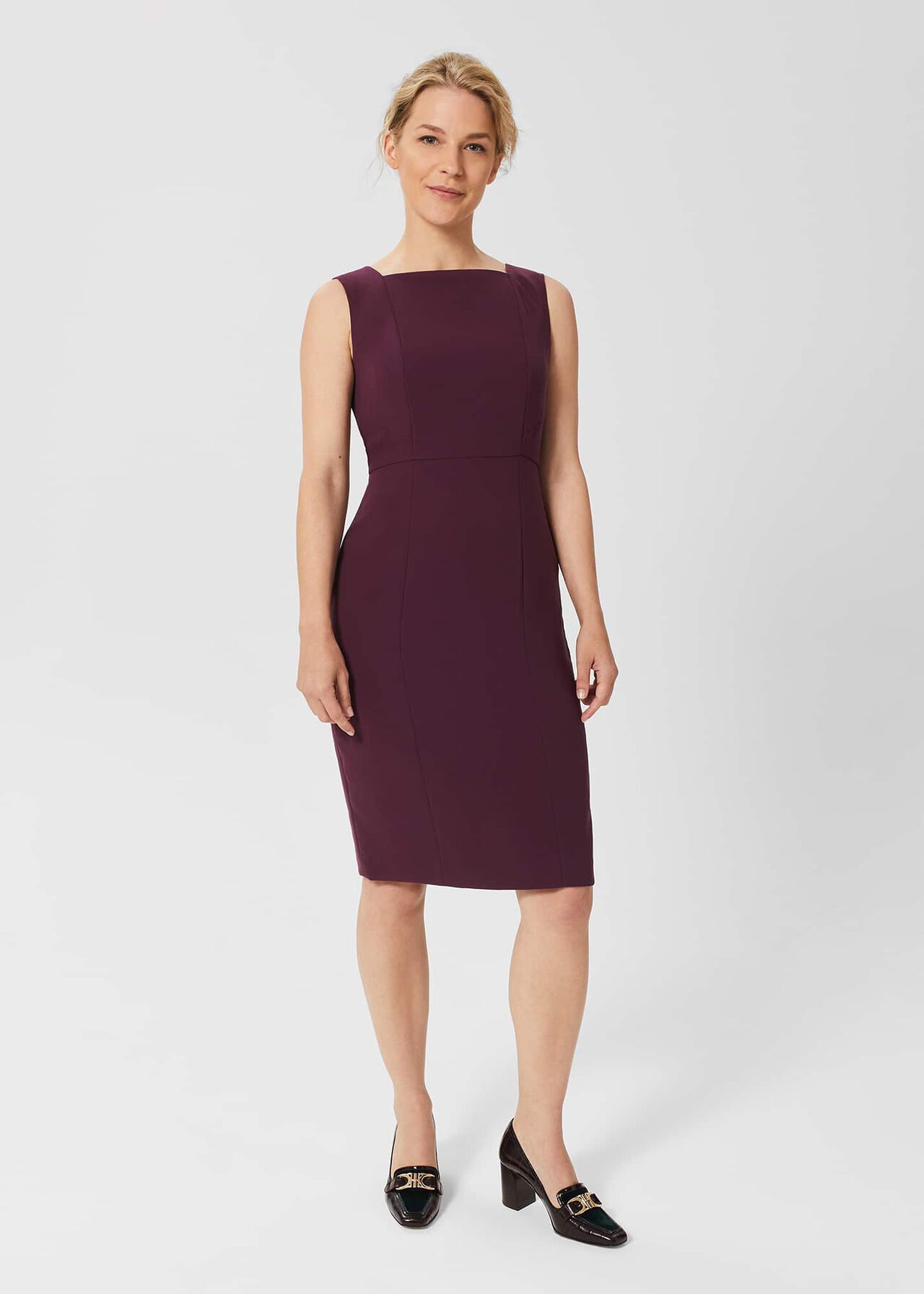 A woman wearing a sleeveless, purple shift dress with seam detailing and a square neckline, standing against a plain background.
