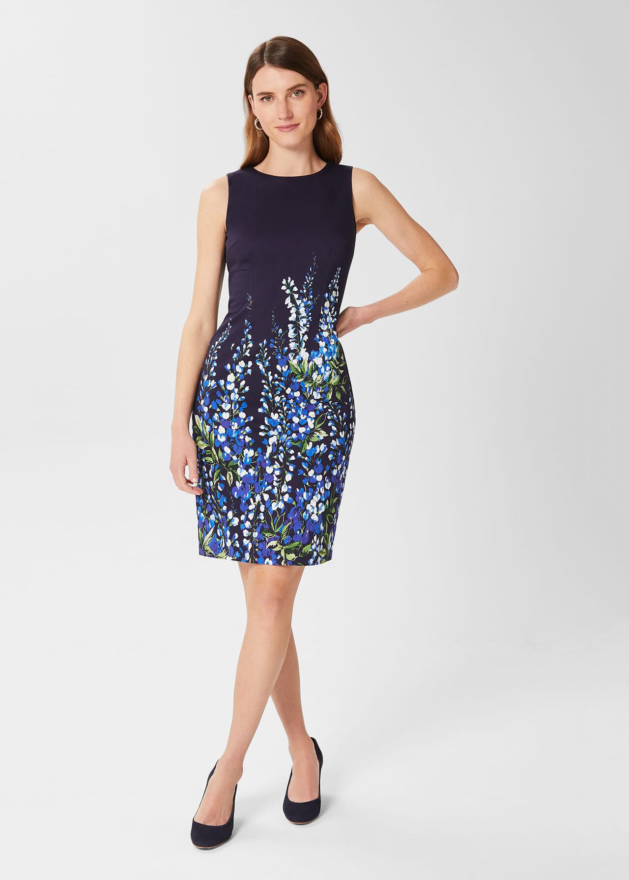 A woman wearing a sleeveless navy shift dress with a vibrant floral print in blue, white, and green, and black high heels.