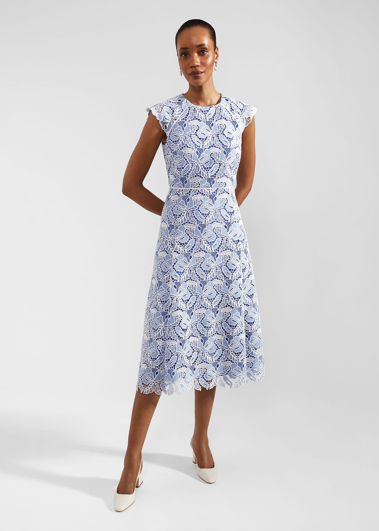 A woman wearing a white and blue lace midi dress with cap short sleeves and a fitted waist, standing against a plain background.