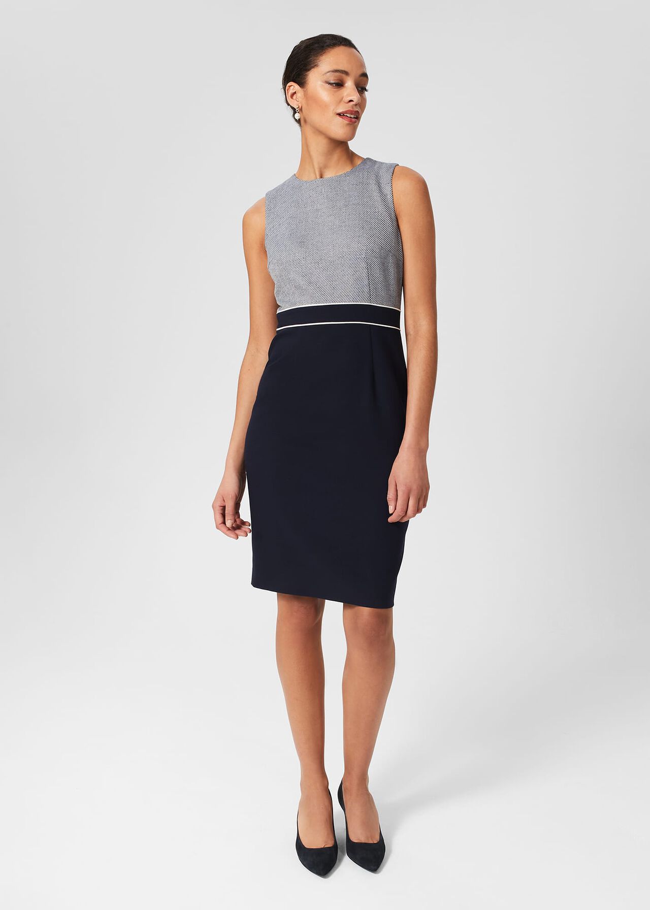 A woman wearing a sleeveless navy and grey dress with a tweed bodice and solid navy skirt, standing against a plain background.