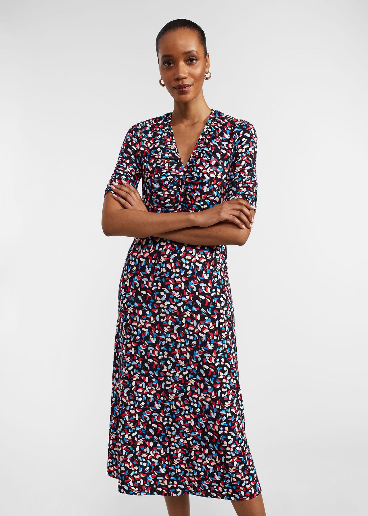 A woman wearing a midi dress with a colorful abstract print, V-neckline, and bracelet-length sleeves.