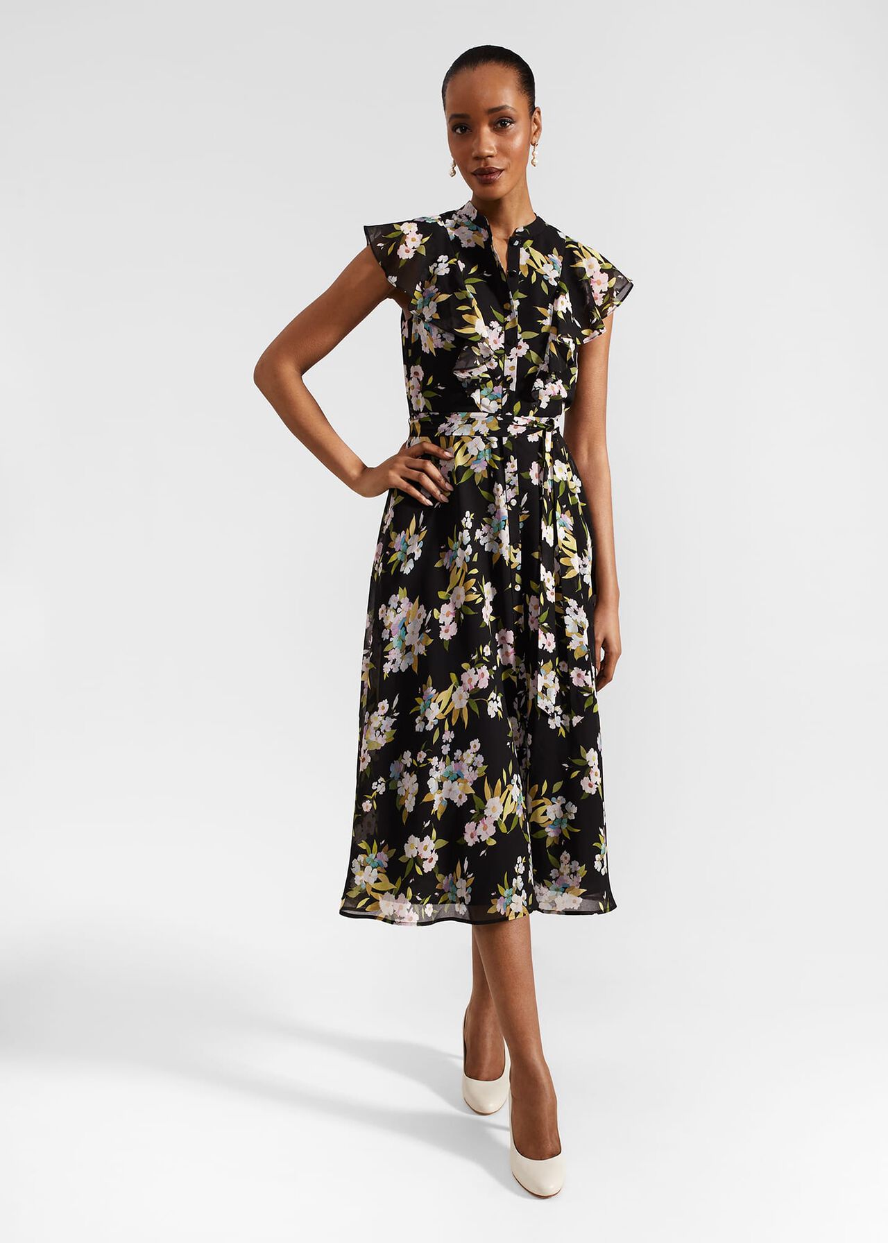 A woman wearing a black floral midi dress with ruffled short sleeves, a belted waist, and a mandarin collar, standing against a plain background.