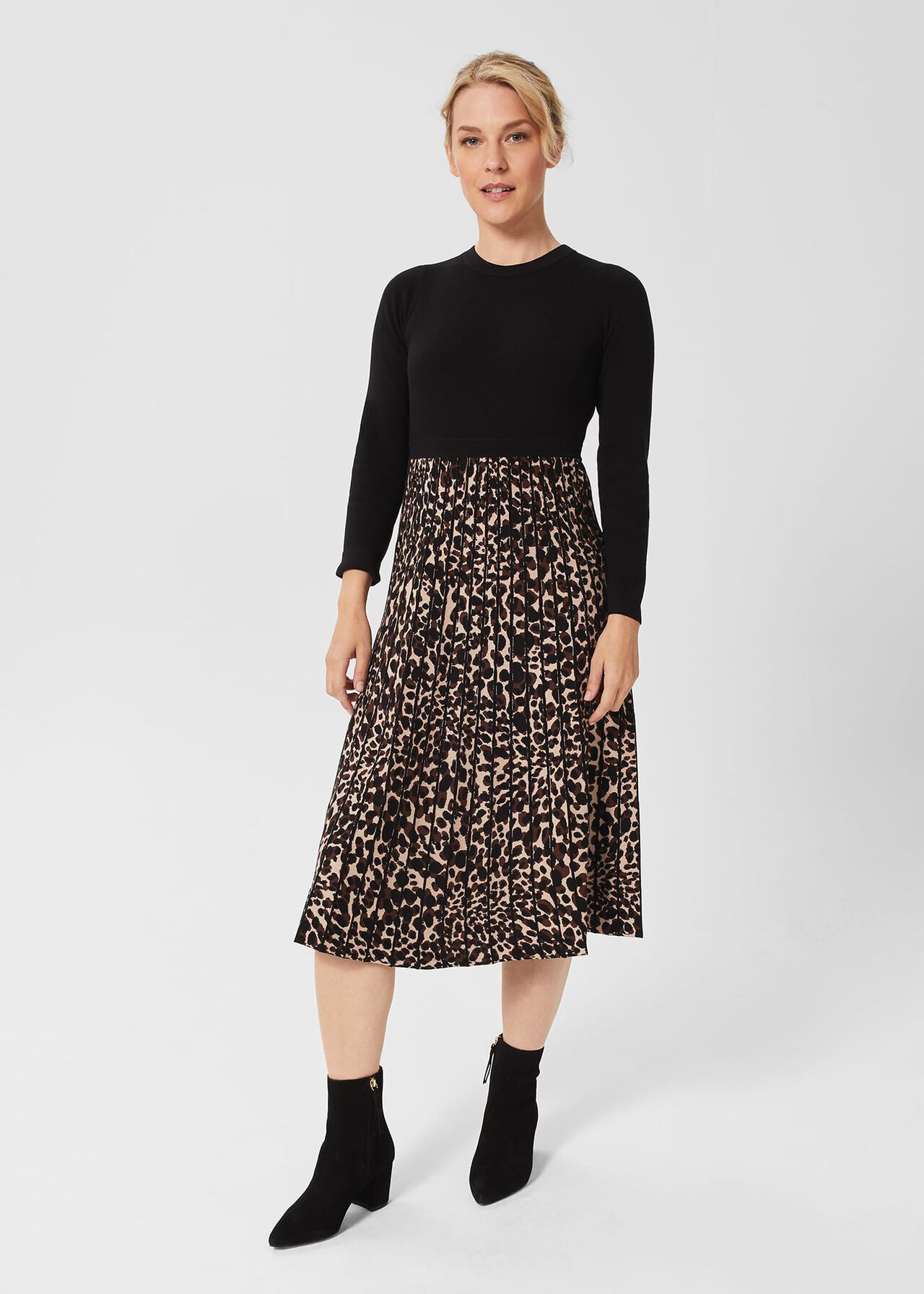 A woman wearing a black long-sleeve top and a leopard print pleated midi skirt, paired with black ankle boots.