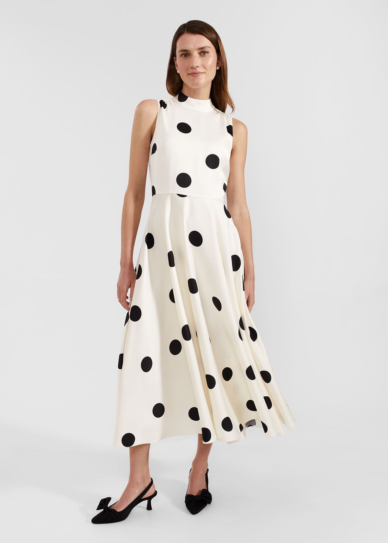 A woman wearing a white polka dot dress with a fitted bodice, flared skirt, and a bow detail at the back.