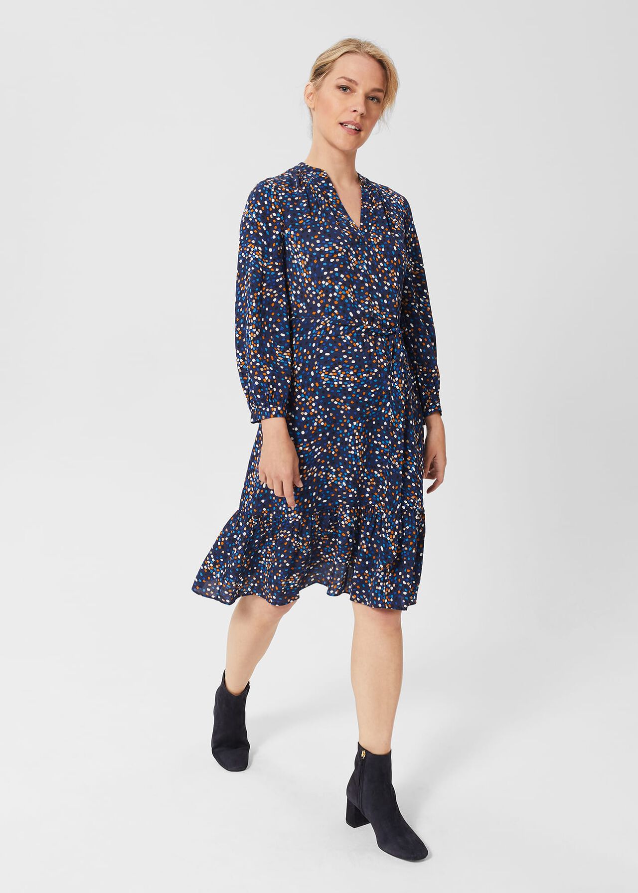 A woman wearing a navy blue dress with a colorful mark-making print, tiered hem, mandarin collar, and long voluminous sleeves.