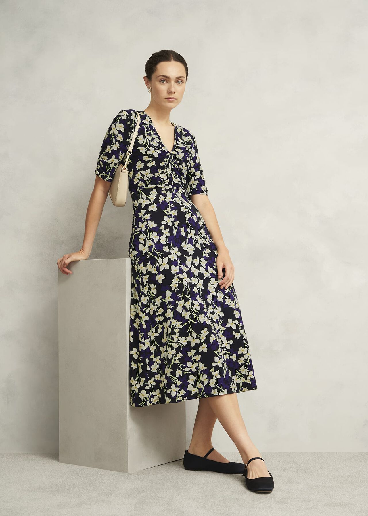 A woman wearing a navy midi dress with a floral print, short sleeves, V neckline, and a fitted waist, standing against a plain background.