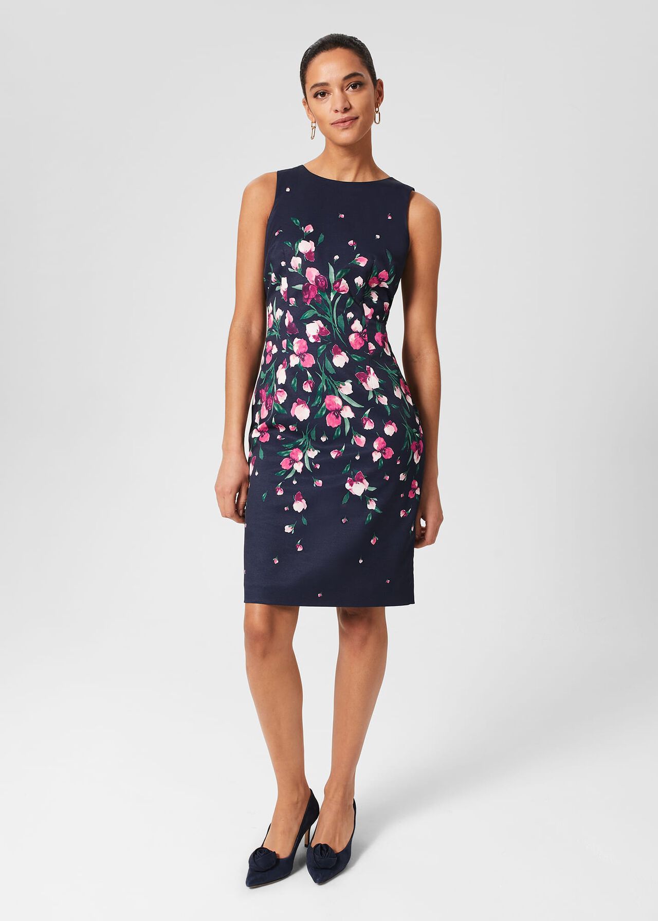 A woman wearing a navy blue floral dress with pink and white flowers, sleeveless, knee-length, with a fitted waist and a round neckline.