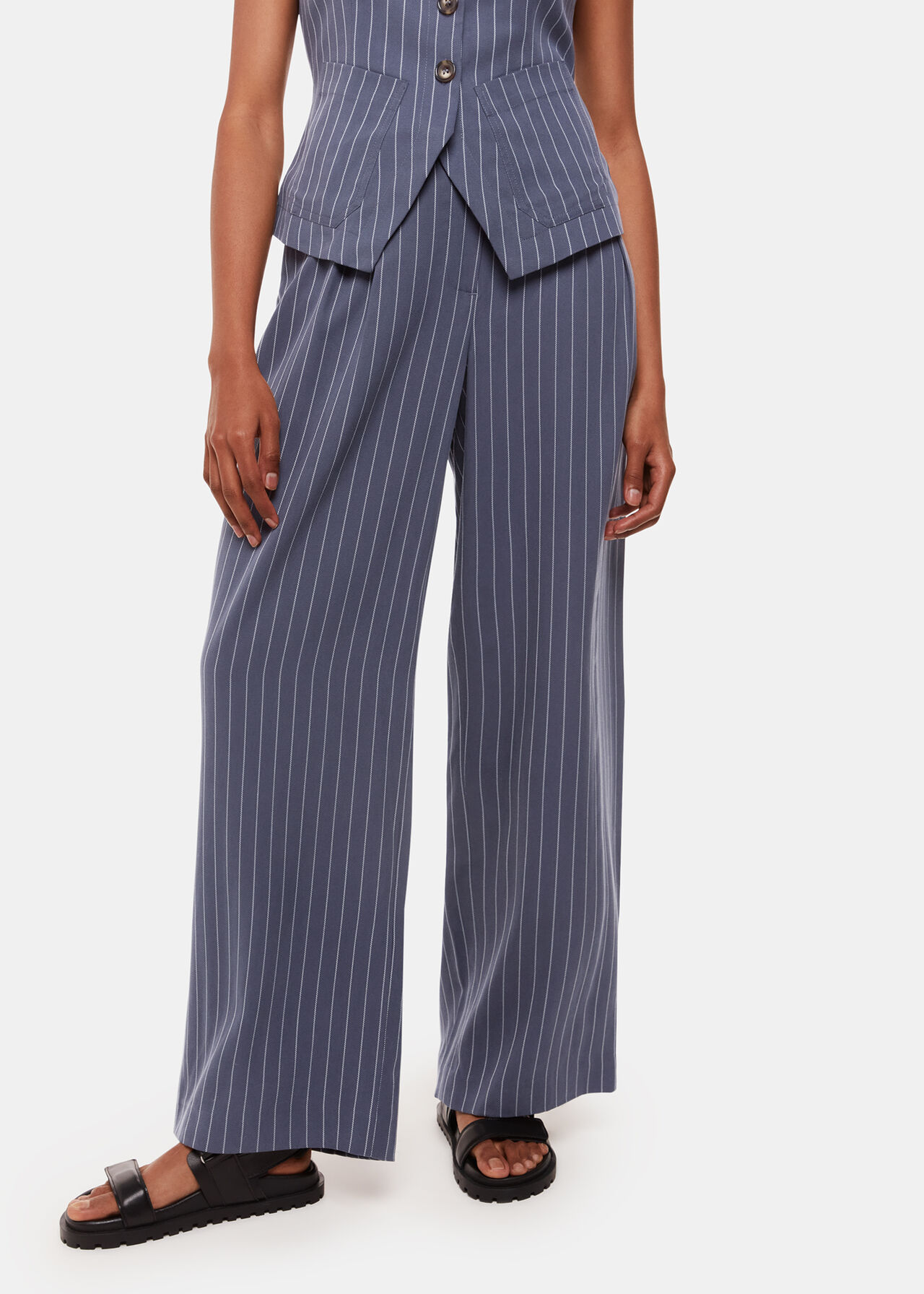 A pair of navy pinstripe trousers with a relaxed fit, fitted waist, side pockets, and pleats, worn by a woman.