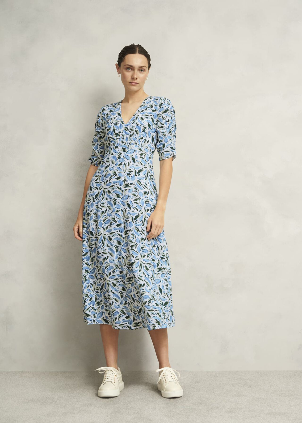 A woman wearing a midi dress with an abstract leaf print in shades of blue, white, and green, featuring a v-neckline and puffed sleeves.