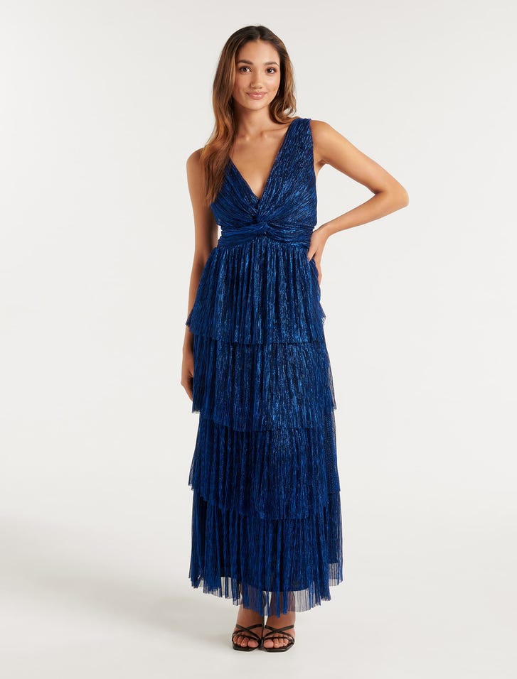 A woman wearing a metallic blue plisse midi dress with a tiered, ruffled skirt, fitted bodice with twist detail, V-neckline, and spaghetti straps.