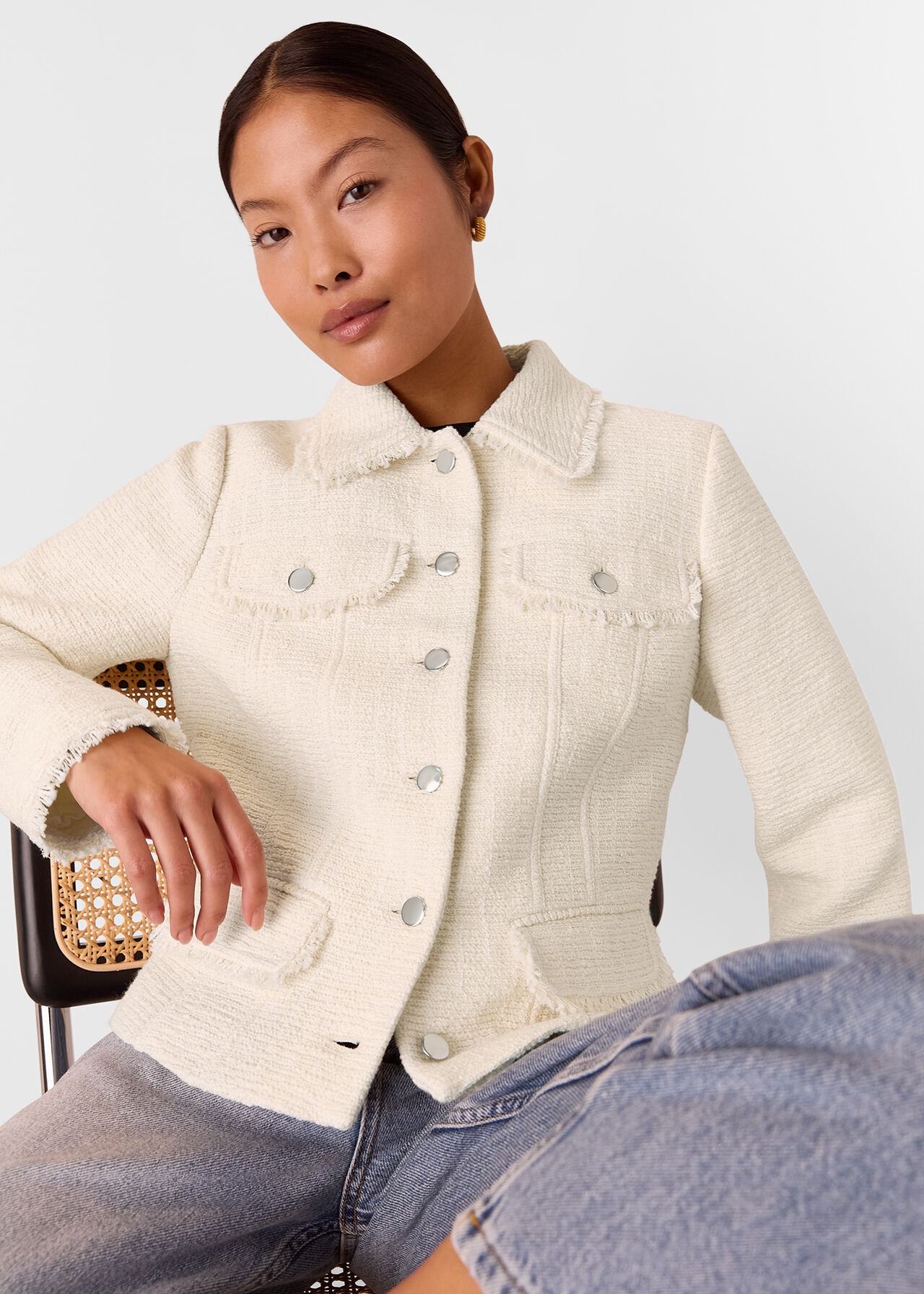 A woman wearing an ivory boucle jacket with a collared neckline, frayed edges, and denim buttons.