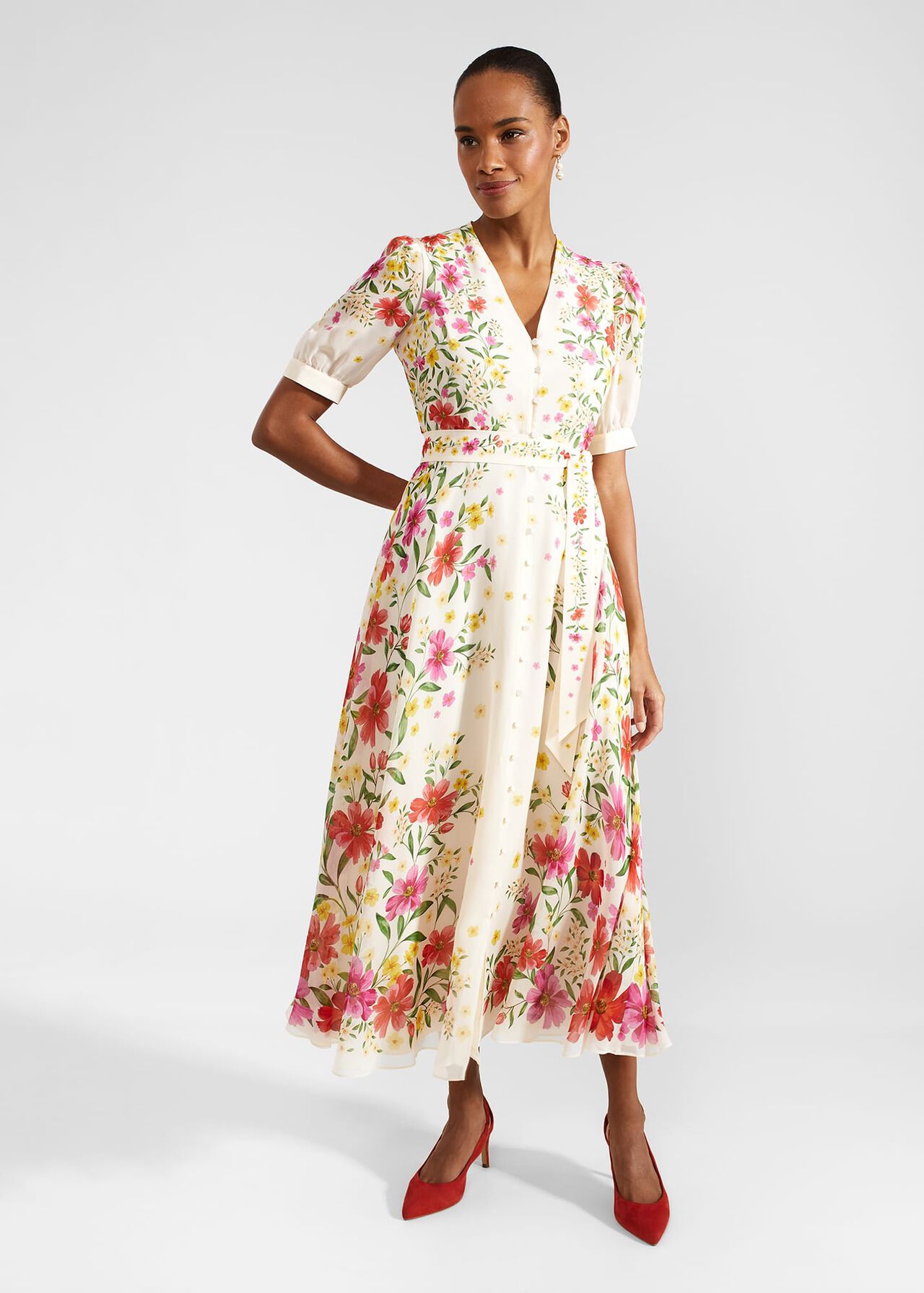 A woman wearing a cream-colored floral silk dress with puff sleeves, a belted waist, and a button front, standing against a plain background.