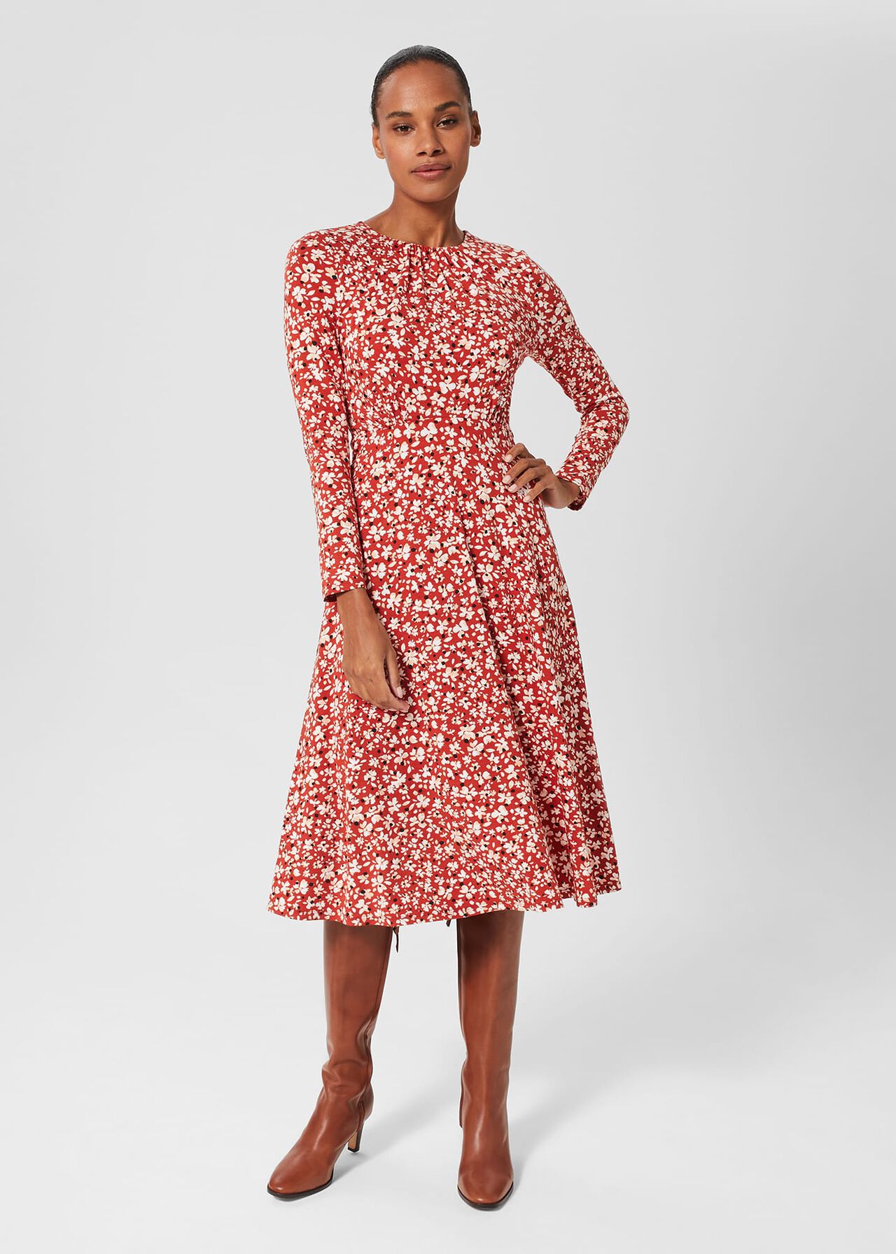 A woman wearing a red floral print dress with long sleeves and a fitted waist, standing against a plain background.