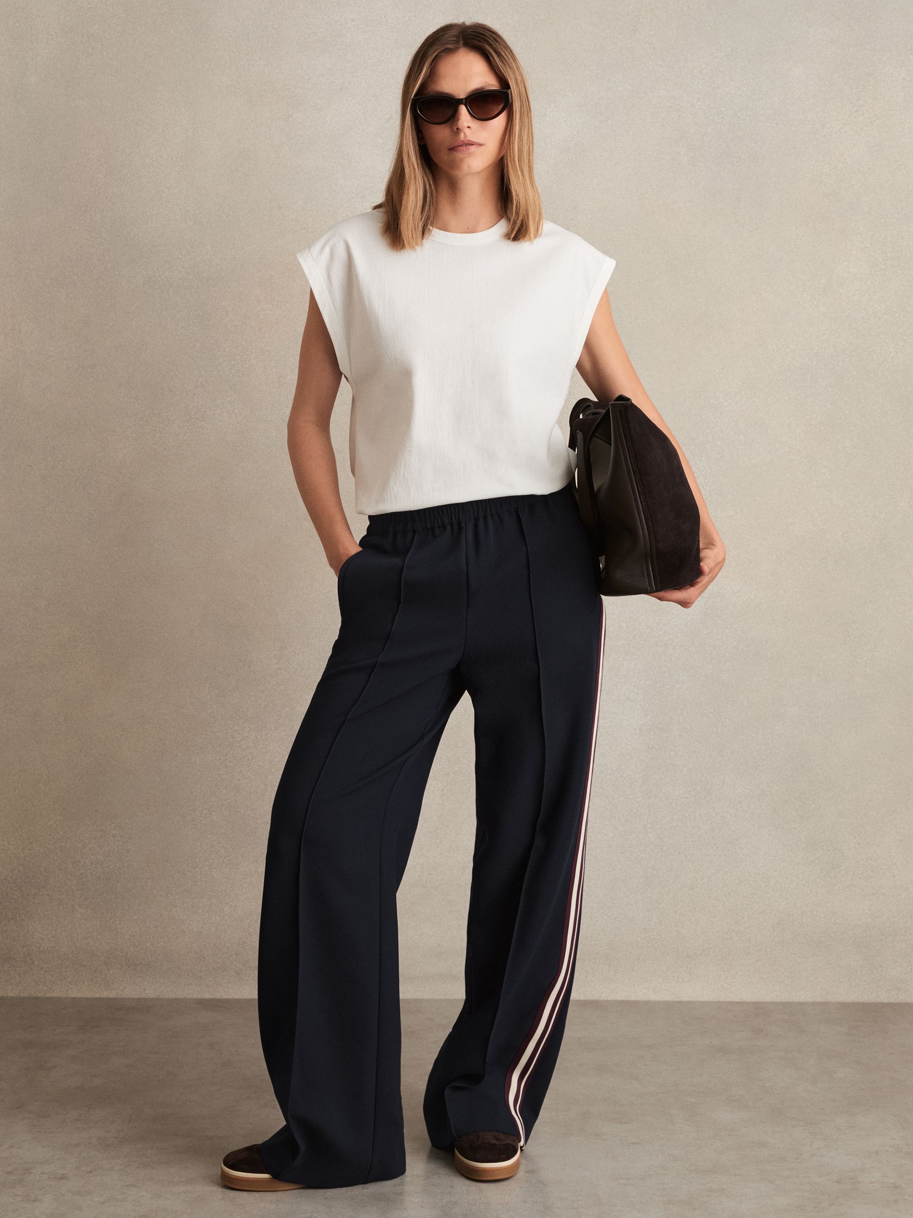 A pair of navy wide-leg trousers with side stripes, elastic waistband, and front pintucks, shown on a model.