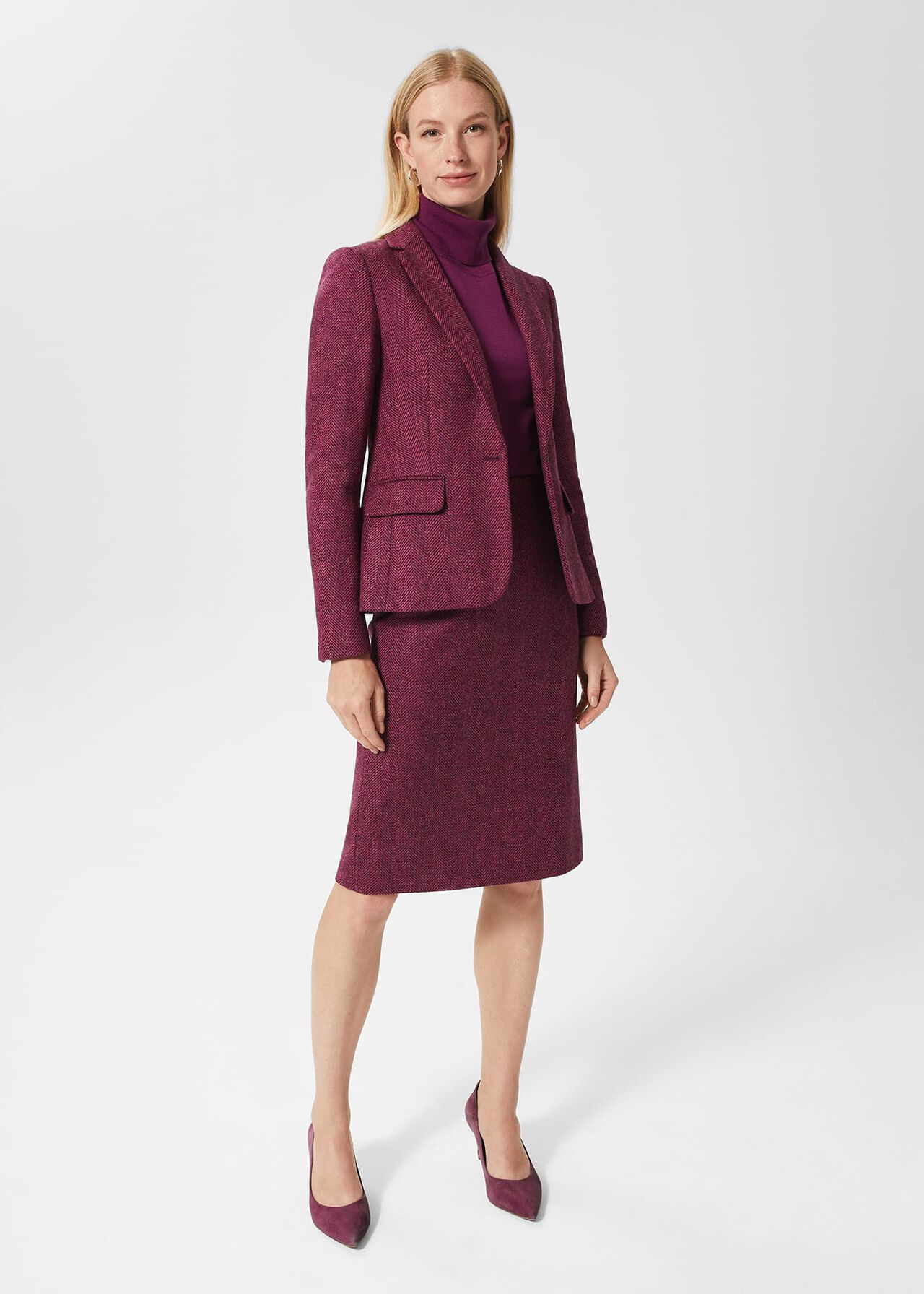 A woman wearing a pinkish-red herringbone check wool jacket with notch lapels, a single-breasted front, and flap pockets.