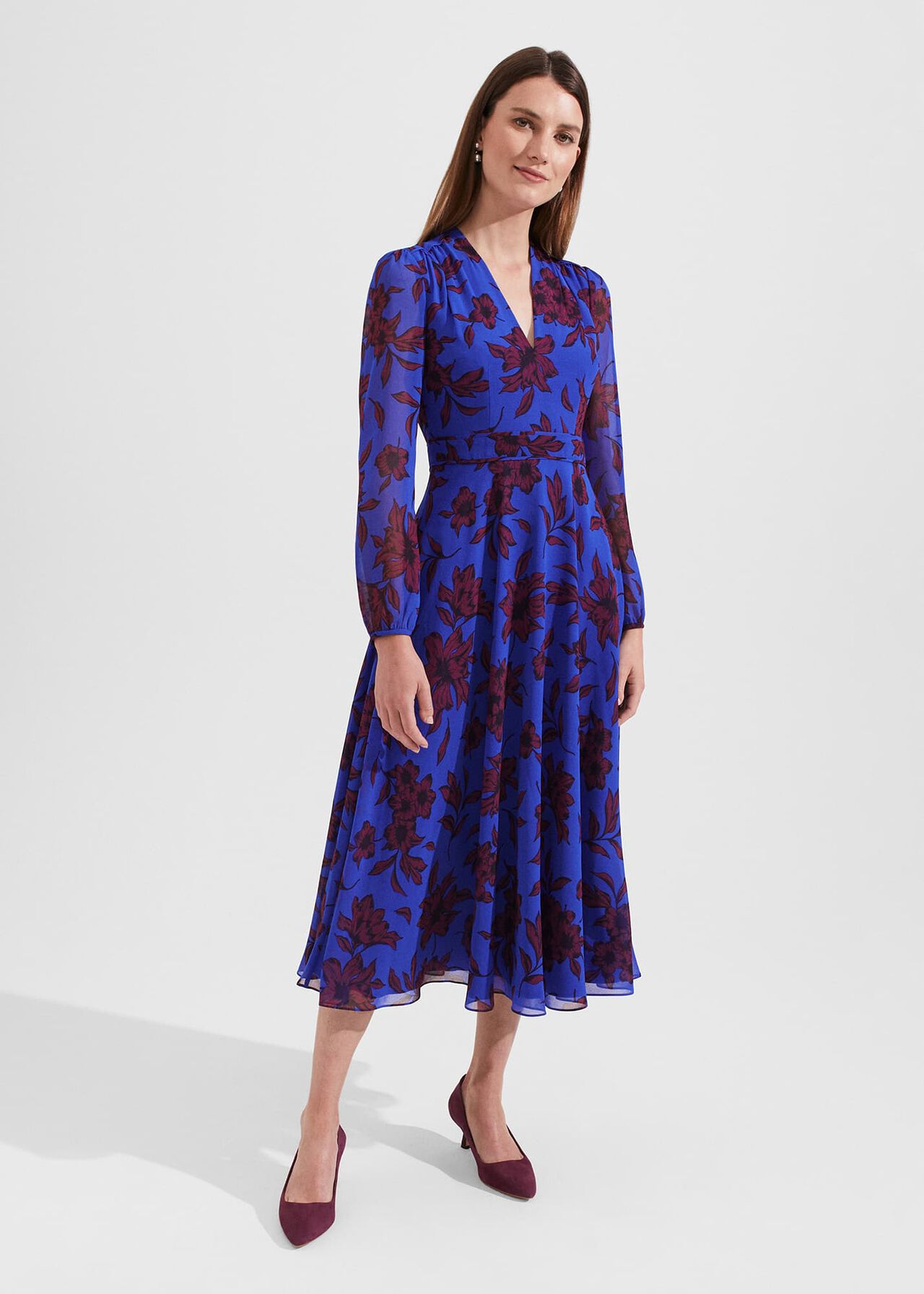 A woman wearing a blue floral fit and flare dress with long sleeves and a V-neckline.