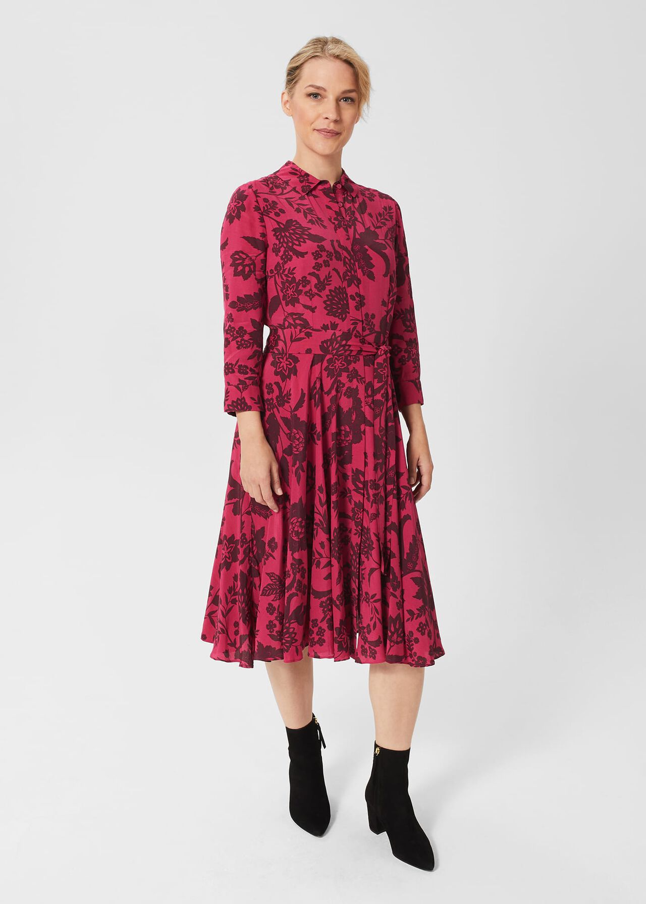 A woman wearing a pink floral print fit and flare dress with a collar, belt, and full skirt.