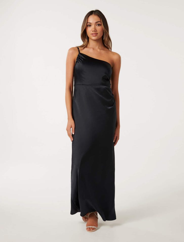 A woman wearing a black satin maxi dress with an asymmetrical one-shoulder neckline, spaghetti straps, and a side split.