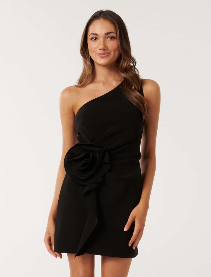 A woman wearing a black mini dress with an asymmetrical neckline and a large rosette detail on the side-waist.