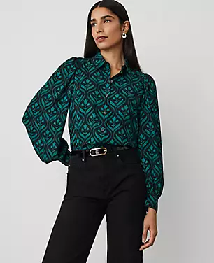 A woman wearing a teal and black geometric patterned collared shirt with puff sleeves, button cuffs, and a pointed collar.