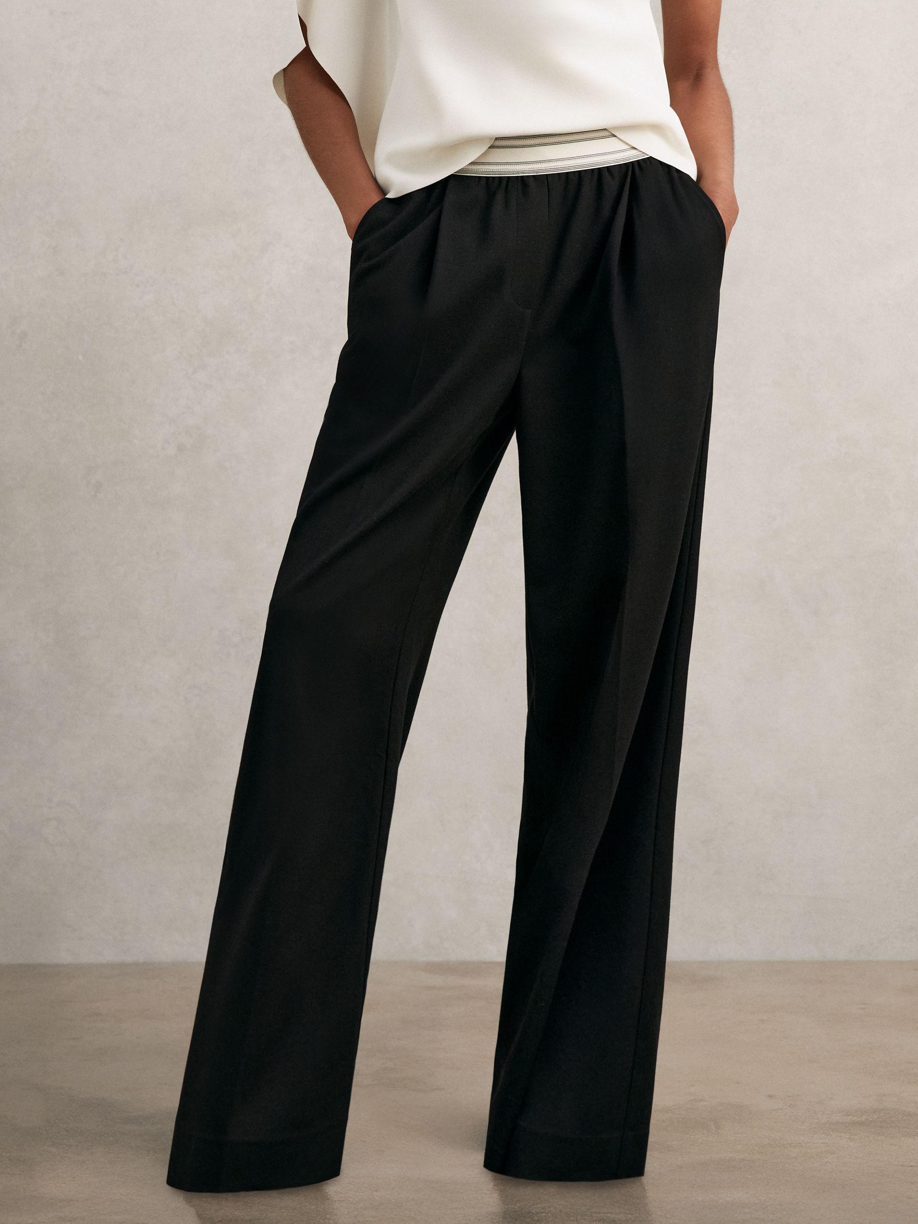 A pair of black petite wide-leg trousers with an elastic waistband and stripe detailing, front pleats, and side pockets.
