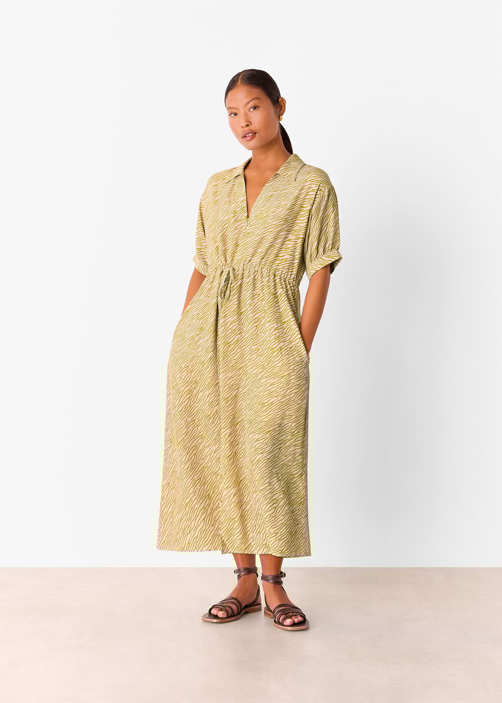 A woman wearing a midi dress with a tiger flame pattern in light green, V-neckline, short sleeves, and a waist belt, standing against a plain background.