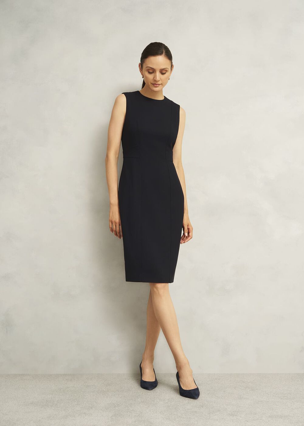 A woman wearing a black sleeveless shift dress with a fitted silhouette, standing against a plain background.