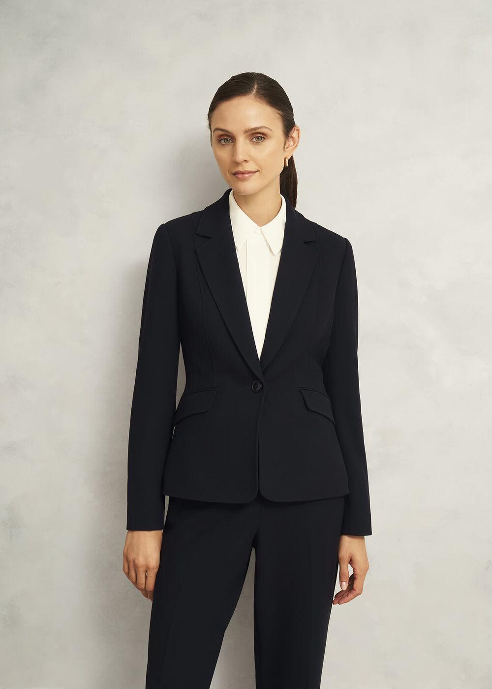 A woman wearing a black tailored blazer with a notch lapel and single-breasted closure, paired with matching black trousers.