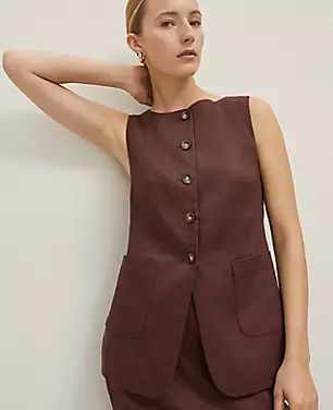 A woman wearing a sleeveless beige vest with a ballet neckline, front buttons, patch pockets, and a back vent, made from linen-twill fabric.