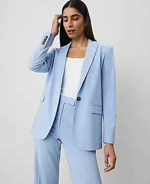 A woman wearing a light blue longline blazer with a peaked lapel, long sleeves with buttons, and front flap pockets.